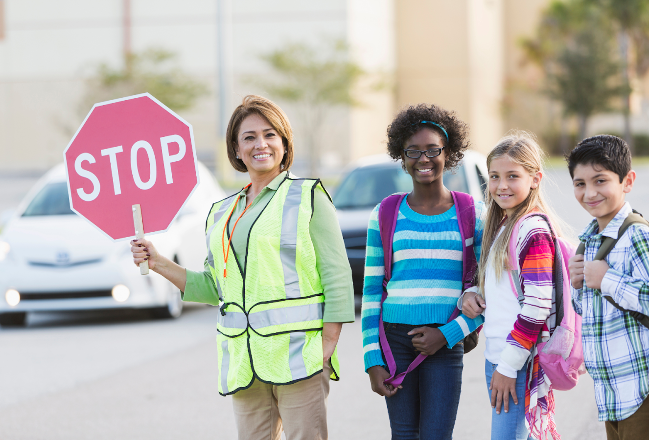 A crossing guard holding a "STOP" sign with children nearby.